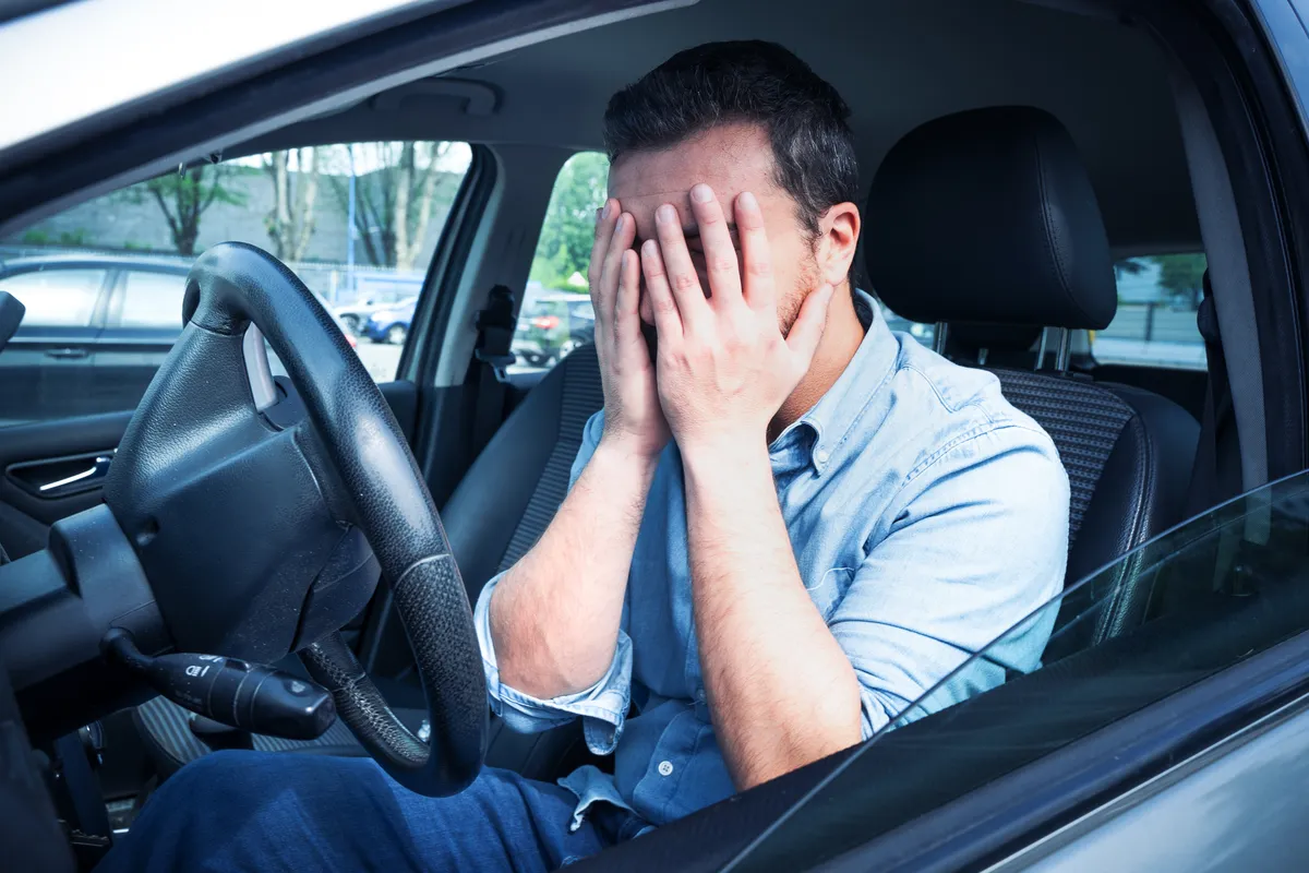 zúfalý muž sediaci v aute ľutuje neuvážené rozhodnutie o kúpe