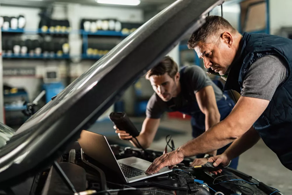 Spolupráca automechanikov v dielni pri vykonávaní diagnostiky vozidla.